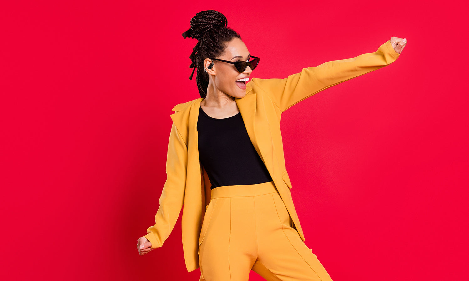Woman in yellow suit wearing translator earbuds, dancing against red background